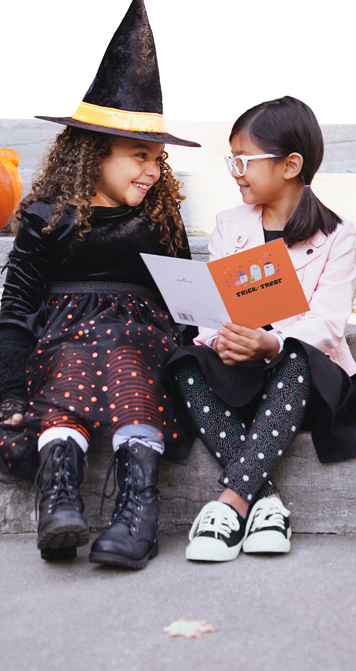 Two young girls in costumes smiling at each other while one holds a Halloween card.